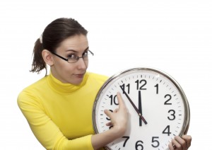 Portrait of an attractive beautiful pretty cute young brown haired caucasian woman (lady, girl, female, person, model) in glasses (spectacles, specs) who is pointing at the clock that shows five to twelve. It's an allegory of the time, appointment, delay, being late, start or finish. Isolated on white background.