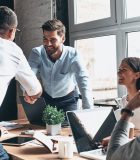 3 reasons why IB is an investment with a high ROI Young modern men in smart casual wear shaking hands and smiling while working in the creative office