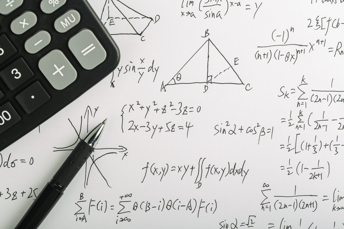 Closeup shot of complex math formulas on paper with calculator and ball pen aside.