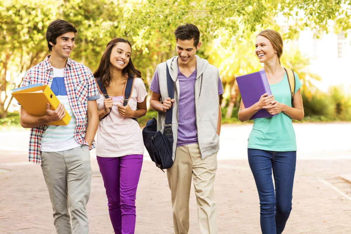 Happy multi-ethnic group of teenage students walking together on university campus. Horizontal shot.