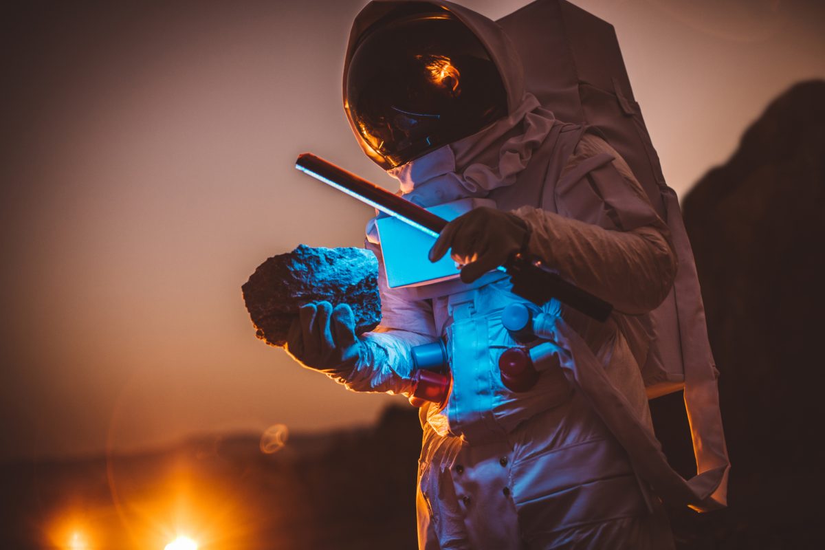 One man, astronaut exploring the land on the other planet at night, holding a lamp.