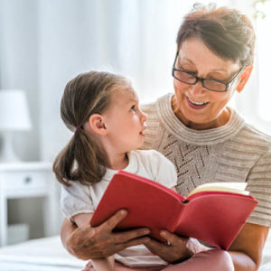 Grandmother reading a book to her granddaughter. Family holiday and togetherness.