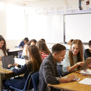 Wide Angle View Of High School Students Sitting At Desks In Classroom Using Laptops