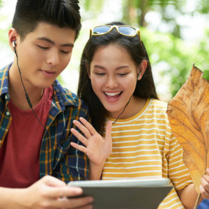 Cheerful Asian young couple with earphones videocalling