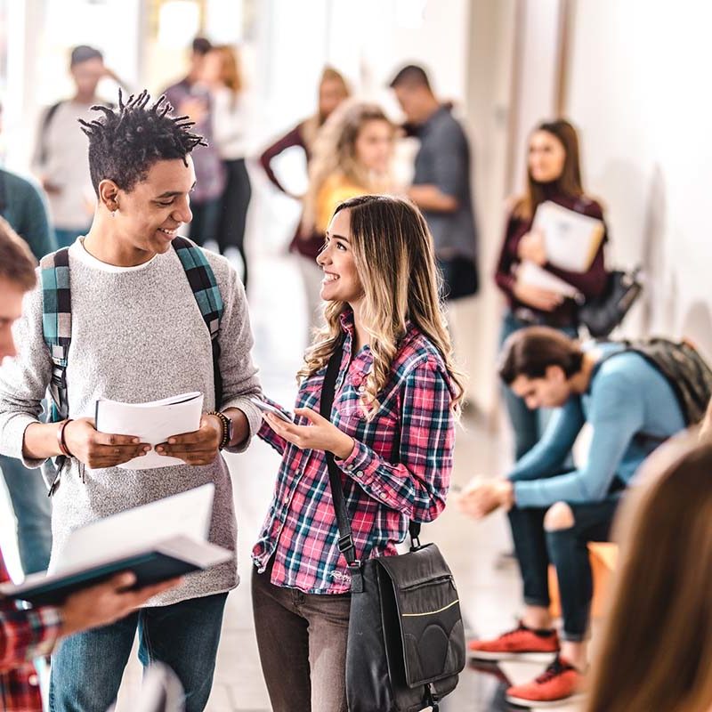 Happy students enjoying in conversation while standing in a hallway of a school building.