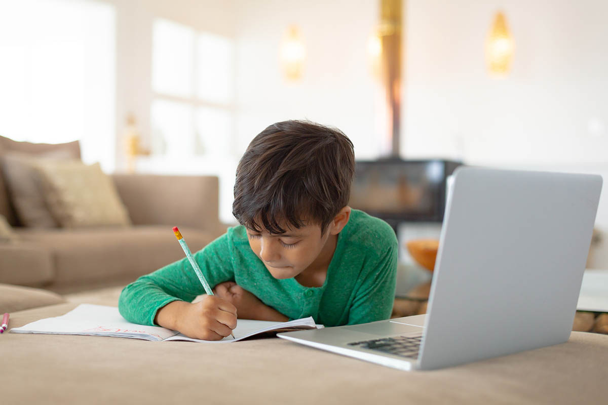 Front view of African american boy using laptop while drawing a sketch on book at home