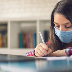 Teenage girl wearing protective face mask and studying at home quarantine due to the epidemic of Coronavirus COVID-19