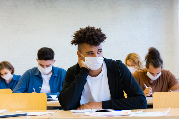 Multiethnic group of students wearing N95 Face masks sitting at the desks in the classroom at the university, keeping distance, having an exam.